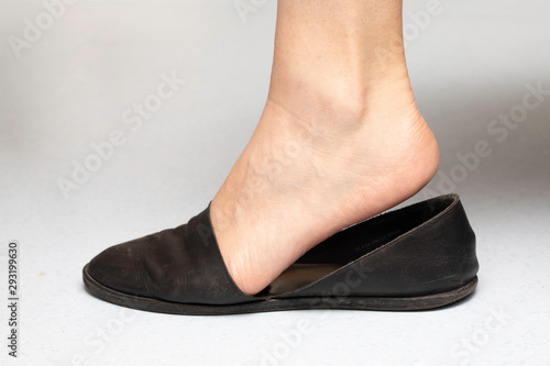 A closeup and side view on the flexed ankle and foot of a caucasian woman slipping into flat bottomed black shoes, common and repetitive movements of the joints cause arthritis and early aging.