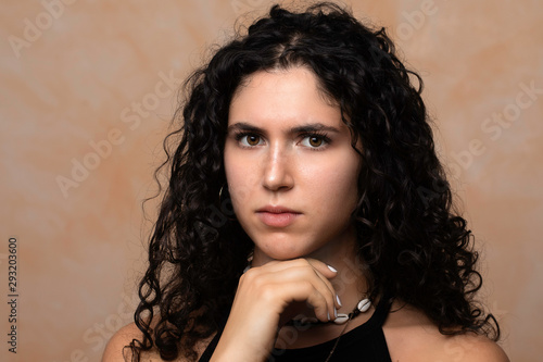 A close up portrait of a stern and serious looking young woman, resting her head on her chin as she stares straight into the camera, confident and empowered.