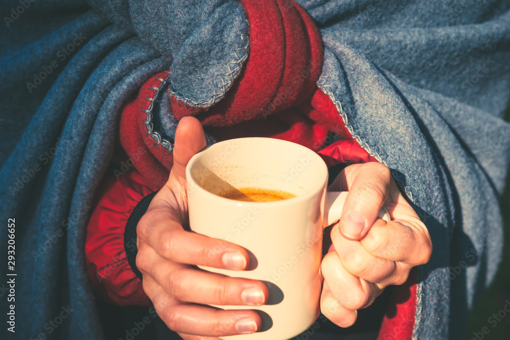 A young girl basks, wrapped in a wool blanket and holding a mug of fresh drink, illuminated by sunlight A young girl basks, wrapped in a wool blanket and holding a mug of fresh drink, illuminated by sunlight