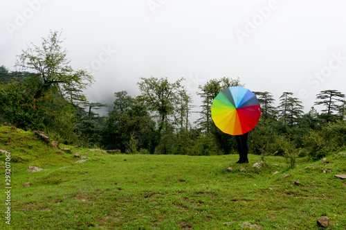 Young indian girl with face hidden holding a colorful umbrella in a foggy feild with fog