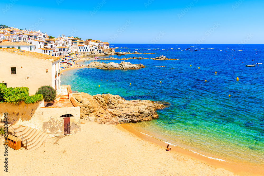 Young woman sitting on sandy beach in picturesque fishing village of Calella de Palafrugell, Catalonia, Spain