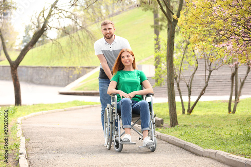 Happy woman in wheelchair and young man at park on sunny day