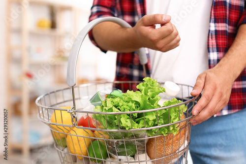 Man with shopping basket full of products in grocery store, closeup