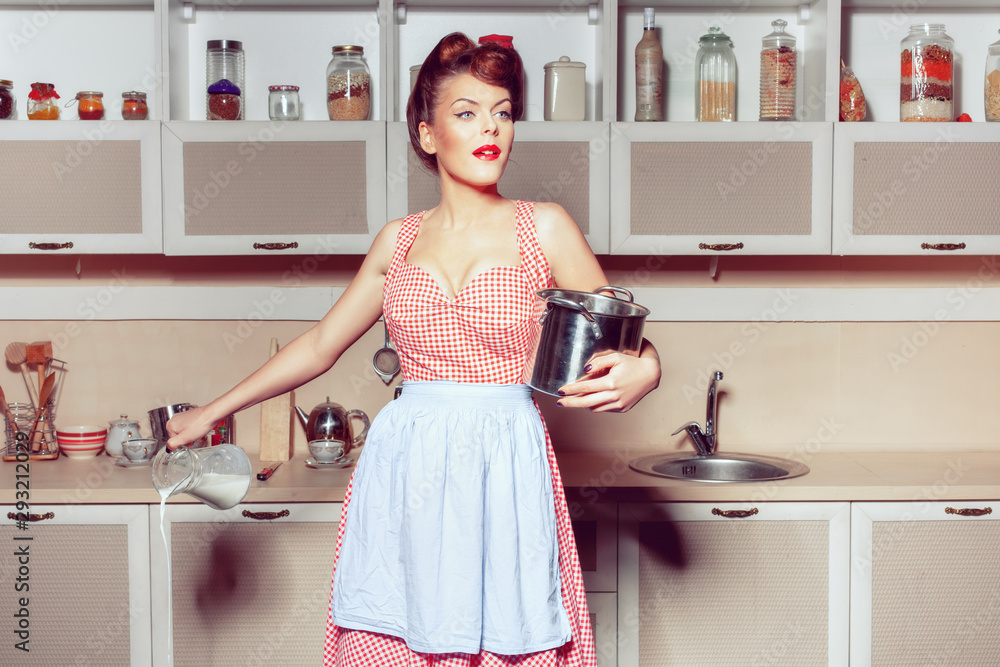 Young woman in the kitchen, she looks surprised. In the woman s hands is a pan and a jug from which milk is poured. Young woman in the kitchen, she looks surprised. In the woman s hands is a pan and a jug from which milk is poured.