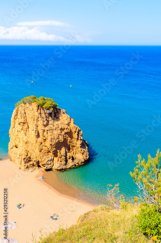 Rock in sea known as Isla Roja on beautiful Cala Moreta beach and view of blue sea, Costa Brava, Catalonia, Spain