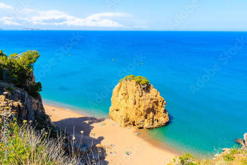 Rock in sea known as Isla Roja on beautiful Cala Moreta beach and view of blue sea  Costa Brava  Catalonia  Spain