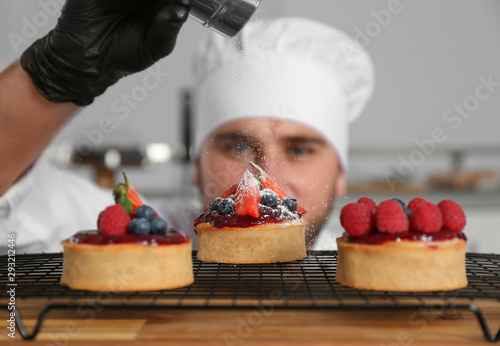 Male pastry chef sprinkling desserts with sugar powder in kitchen photo