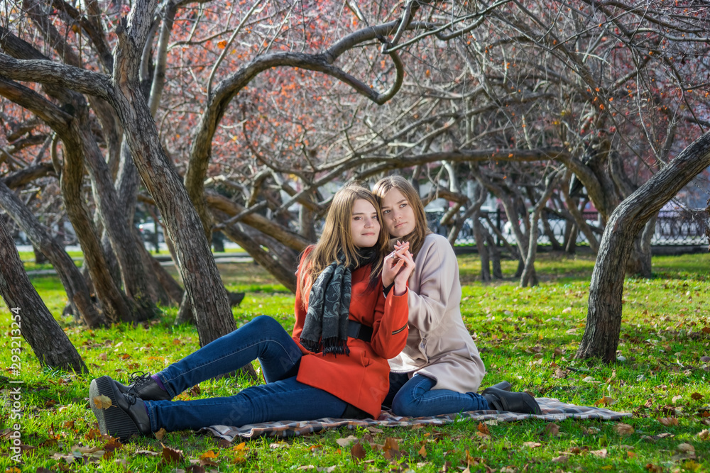 Two pretty girlfriends are sitting on lawn in park Two pretty girlfriends are sitting on lawn in park