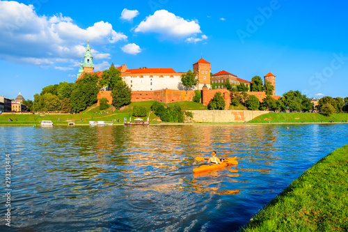 Unidentified young woman paddling in yellow kayak on Vistula river with Wawel castle in background, Krakow, Poland