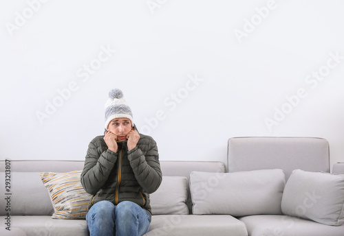 Young man wearing warm clothes freezing on sofa at home. Air conditioner malfunction