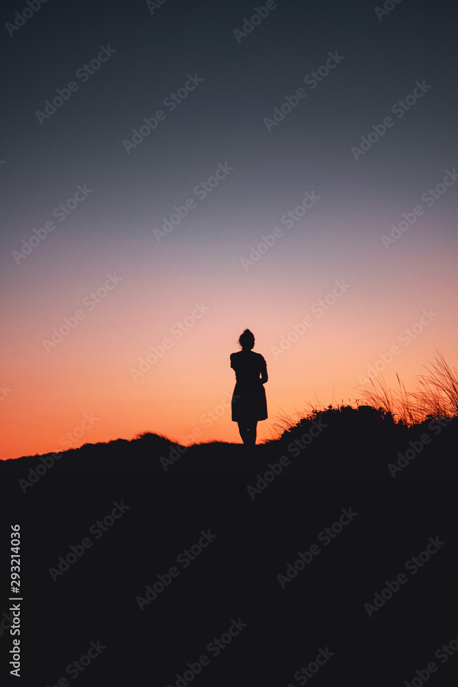 A calm and peaceful with a girl standing on the beach an waves with perfect sunset reflection on a holiday evening. Praia da Bordeira at the Algarve Coast in Portugal, Atlantic Ocean