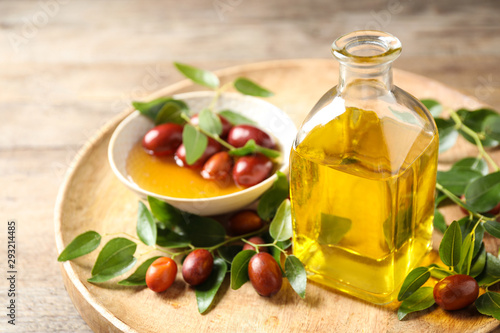 Glass bottle with jojoba oil and seeds on wooden table