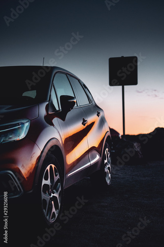 A car parked at the beach in beautiful colorful summer sunset light with reflection in the sculptural body. Vacation trip on a road trip. Lagos, Faro, Portimão, Algarve coast in Portugal, Atlantic
