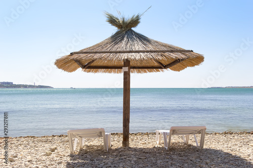 Fototapeta Naklejka Na Ścianę i Meble -  Vacation background. Big umbrella in a center and two loungers on a beach. View from behind. Sunny day.