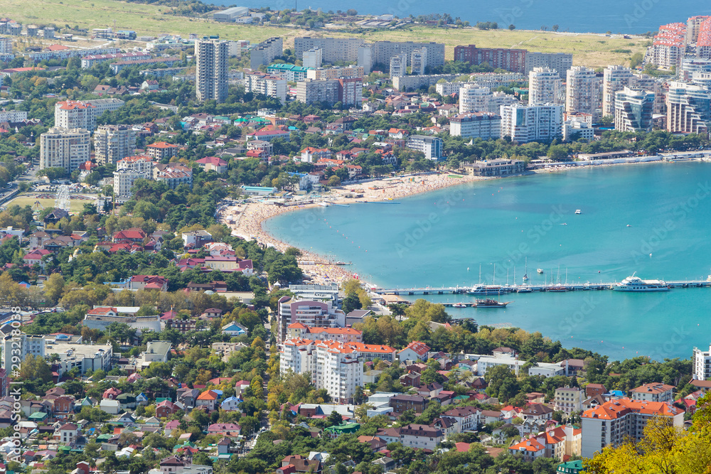 Fototapeta premium Resort town. Bird's-eye view. Sunny day in Gelendzhik. Turquoise water of the sea bay and sand beach with many people in frame. Velvet season.