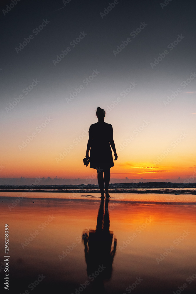 A calm and peaceful with a girl standing on the beach an waves with perfect sunset reflection on a holiday evening. Praia da Bordeira at the Algarve Coast in Portugal, Atlantic Ocean