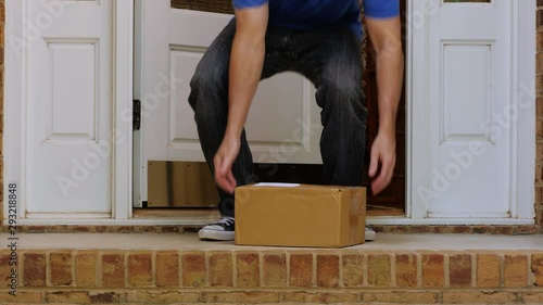 Man opening front door and picking up package delivered to the doorstep. Retrieving shipment parcel box from porch of house.