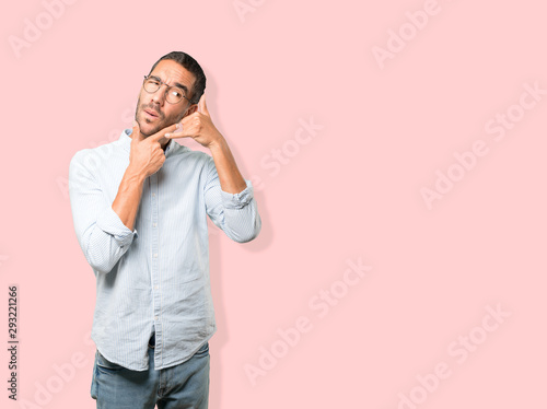 Hesitant young man making a gesture of calling with the hand