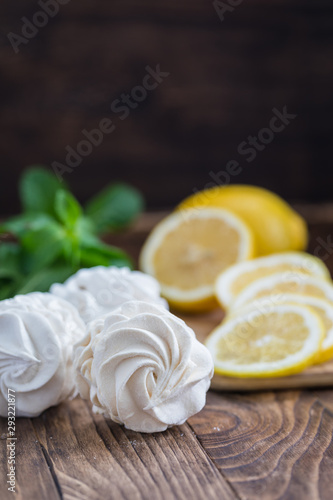 Yellow and white russian marshmallows zephyr on wooden table with lemon slices and mint leaves to show the flavour