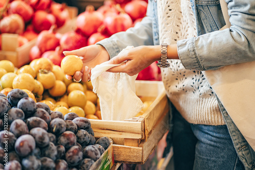 Fotografie Female hands puts fruits and vegetables in cotton produce bag at food market