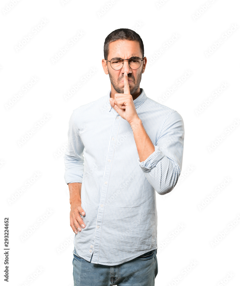 Serious young man asking for silence gesturing with his finger Serious young man asking for silence gesturing with his finger