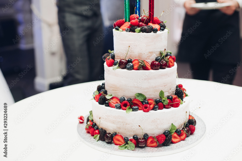 Close-up of a beautiful white cream cheese wedding cake decorated with delicious fresh berries on each layer. Decorated with strawberry, blueberry, cherry and blackberry. Close-up of a beautiful white cream cheese wedding cake decorated with delicious fresh berries on each layer. Decorated with strawberry, blueberry, cherry and blackberry.