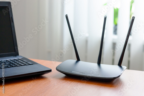 wireless wifi router and laptop at wooden table indoors. window behind. wireless connection concept photo
