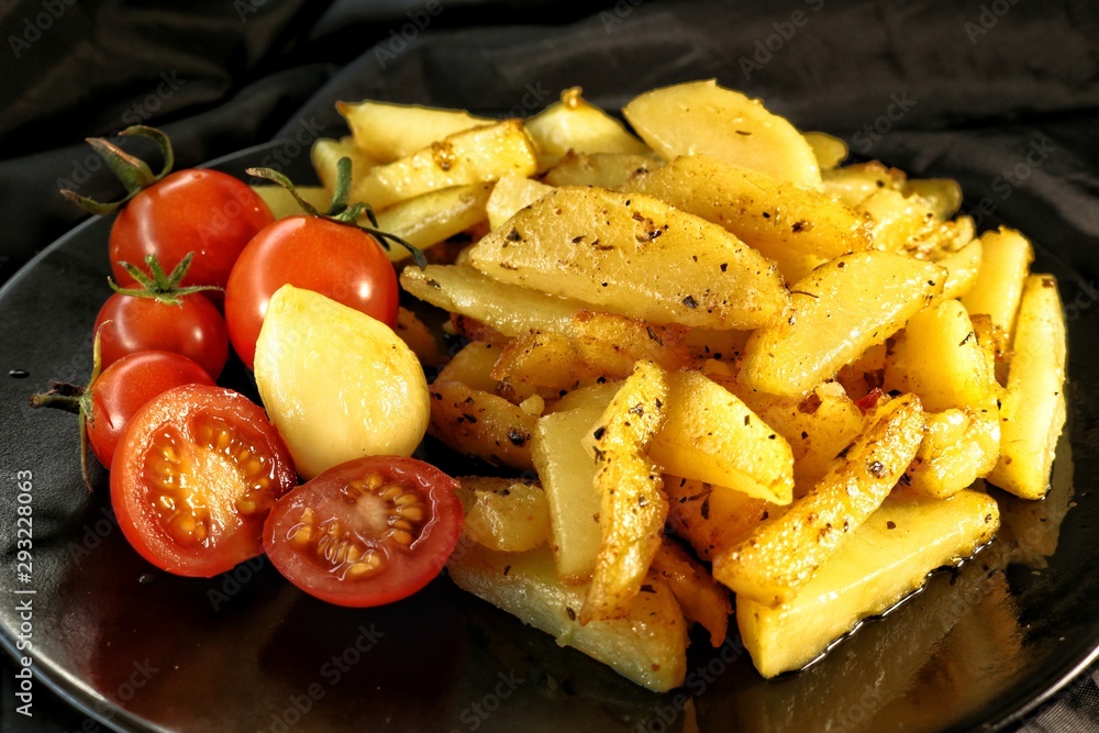fried potatoes with crust, spices, garlic and fresh cherry tomatoes on a black plate fried potatoes with crust, spices, garlic and fresh cherry tomatoes on a black plate