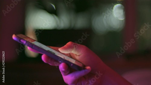 Gadget technology or communication concept : Close up woman hands using smart phone in dark room in front of computer monitor.