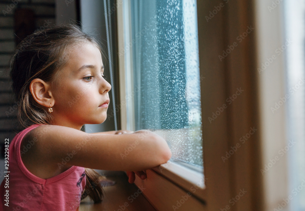 Little sad girl pensive looking through the window glass with a lot of raindrops. Sadness childhood concept image. Little sad girl pensive looking through the window glass with a lot of raindrops. Sadness childhood concept image.