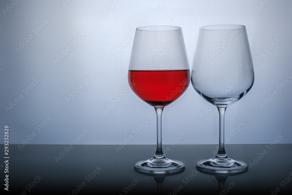one glass half full of red wine, and the second empty on a white background. one glass half full of red wine, and the second empty on a white background.