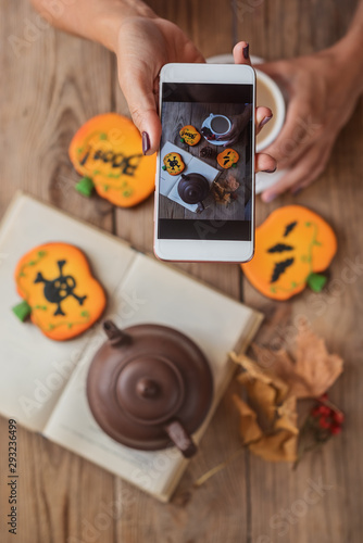 Woman hands photographing a table with Halloween biscuits and coffee on their phone