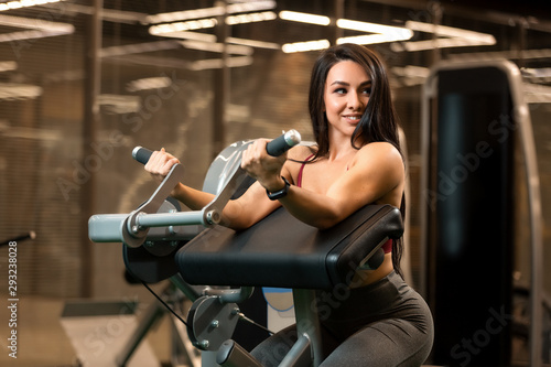 Sexy fitness brunette girl is sitting and doing biceps curls on trainer
