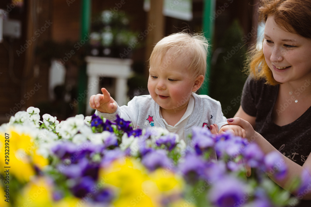 One year old exploring flower shop with her mother. Touching and smelling colorful pansies.