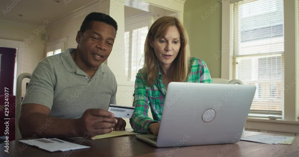 Mature Husband and Wife using laptop computer to make online purchase with credit card. African American and Caucasian couple paying using laptop computer for online banking. Slow motion 4k handheld Mature Husband and Wife using laptop computer to make online purchase with credit card. African American and Caucasian couple paying using laptop computer for online banking. Slow motion 4k handheld