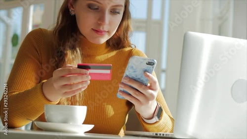 On a Sunny Day. Beautiful Sunny Day Young Woman Drinks Morning Coffee in a Cafe, Making Online a Purchase Easy Payment on the Internet Using a Mobile Phone or Laptop. photo