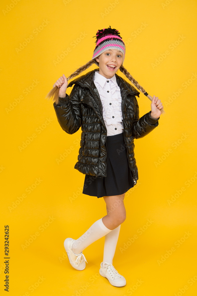 Warm clothing. Buy clothes for school season. Schoolgirl fashion outfit. Fall autumn winter. Fancy little child. Fashion shop. Girl wear knitted hat and down jacket yellow background. Fashion concept ...