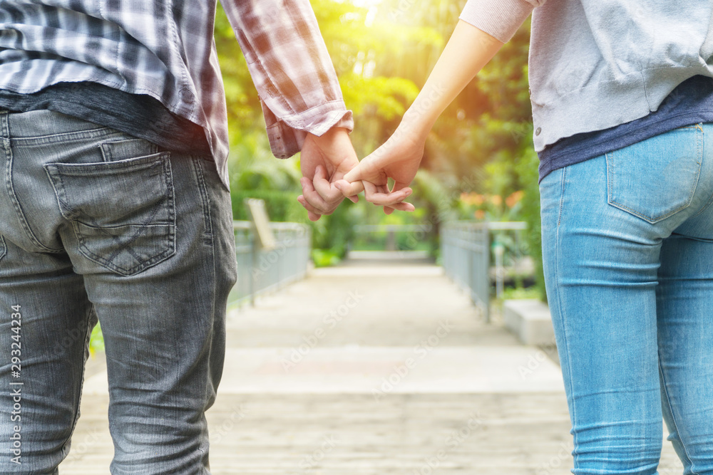 Hands of young couple wear jeans holding finger crossed with wood bridge background. Romantic handsome young man holding hand his girlfriend while standing in the park. relationship concept.
