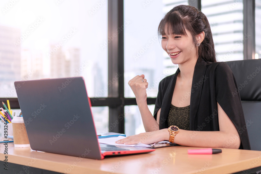 Accountant young woman sitting in coworker while looking at laptop, She raised fist up feeling cheer success her project. Joyful businesswoman with notebook on desk in workplace successful her job. Accountant young woman sitting in coworker while looking at laptop, She raised fist up feeling cheer success her project. Joyful businesswoman with notebook on desk in workplace successful her job.