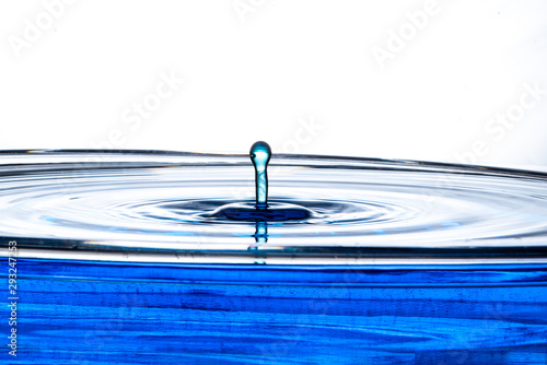 Single drop of water rises out of a calm pool surface into a leaning bulb column to the left.