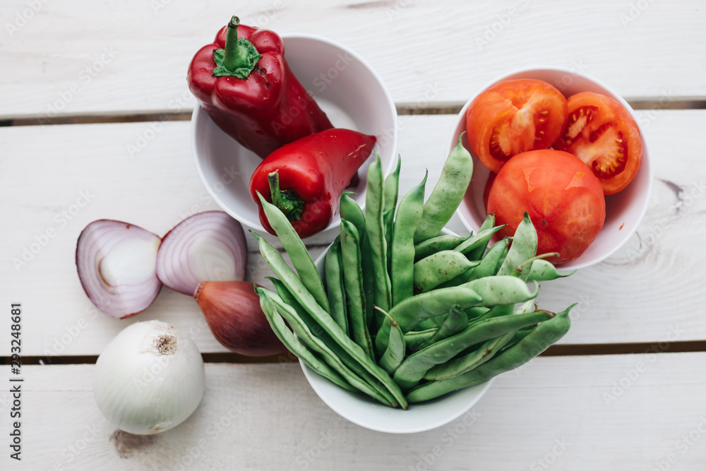 Fresh green beans, red pepper, tomatoes and onions in bowls on white background