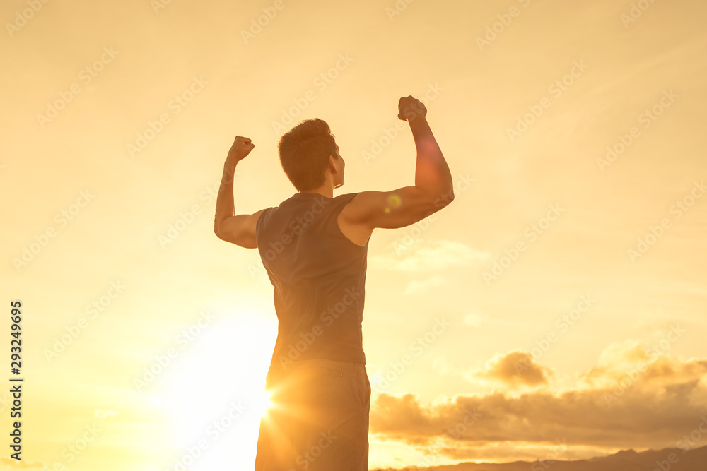 Strong confident man flexing his arms facing the sunset. 