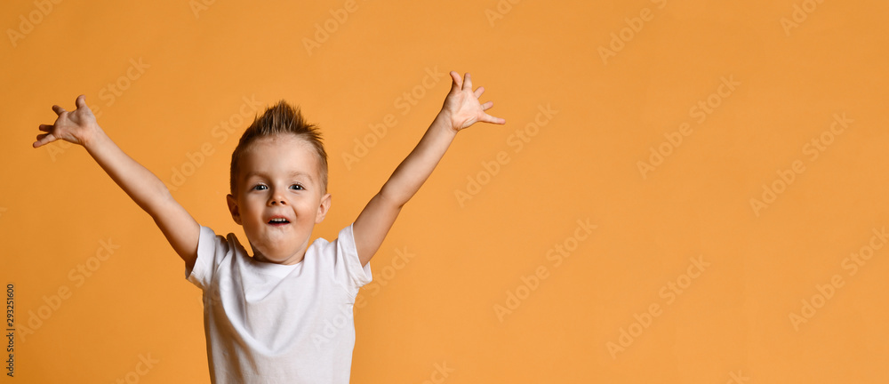 Young boy kid in white t-shirt celebrating happy smiling laughing with hands spreading up on yellow - obrazy, fototapety, plakaty 