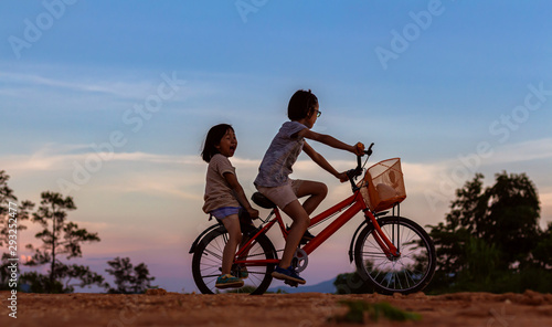 Silhouette two children playing riding bike on mountain at sunset sky background