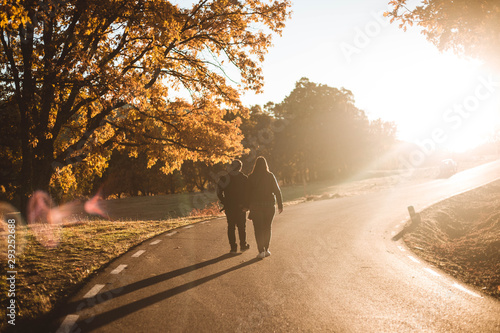 Young couple walking along asphalt road in colorful autumn beech and oaks forest. Autumn road in mountains. Love and nature concept.