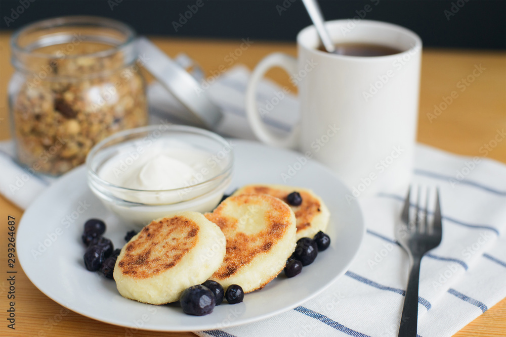 eastern european breakfast, fried circular syrniki, tvorozhniki or cheese cake with sour cream and hot drink on wooden table, close up view from above of horizontal still life stock photo image
