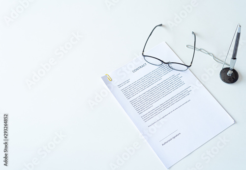White table with paper contract detail and empty space to sign authorized signature, props with glasses and ink pen, copy space available for text
