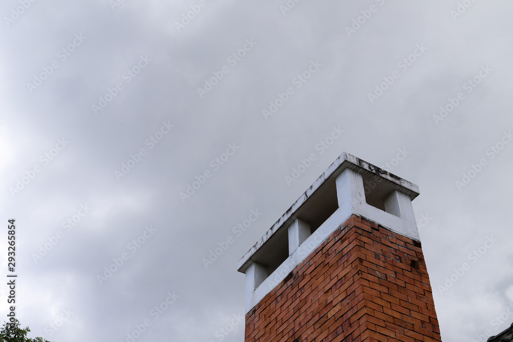 Closeup of brown brick chimney with dark white cloudy sky.