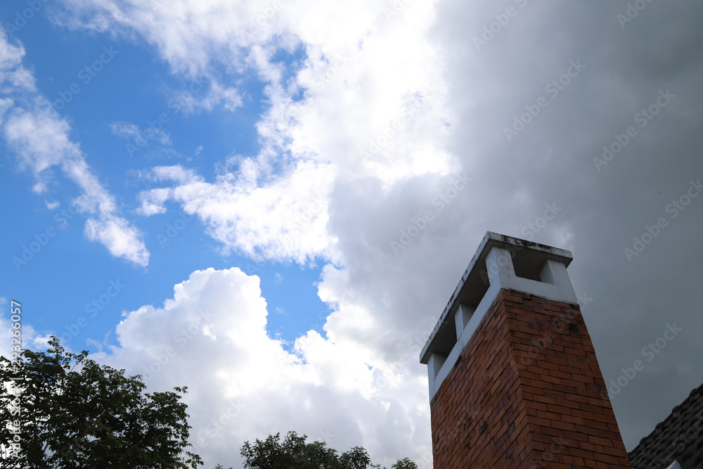 Closeup of brown brick chimney with dark white cloudy blue sky and sunlight. 