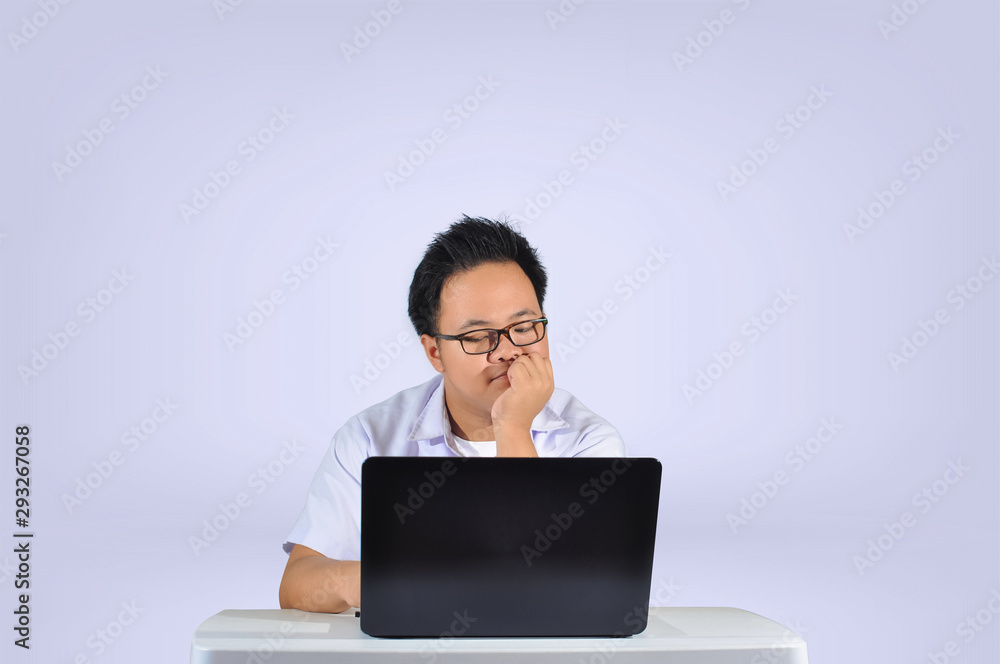 A young Asian student wearing white polo school uniform with eye glasses thinking and analyzing while looking at his laptop screen in white isolated background. A young Asian student wearing white polo school uniform with eye glasses thinking and analyzing while looking at his laptop screen in white isolated background.